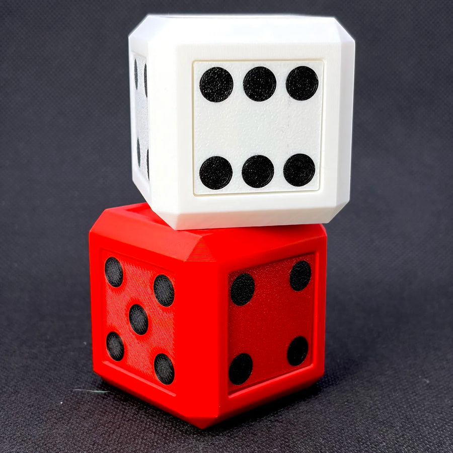 Two 3D-printed dice stacked on top of each other, with a white die on top showing six pips and a red die below showing five pips, set against a dark textured background.