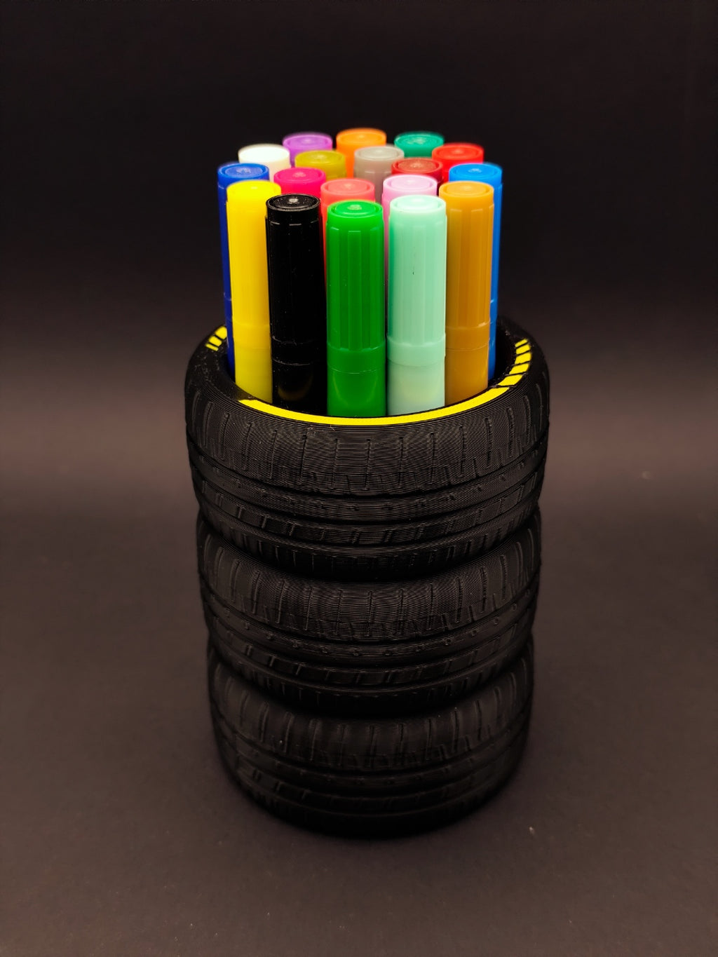 Stacked tire pen holder displaying colorful markers against a dark background