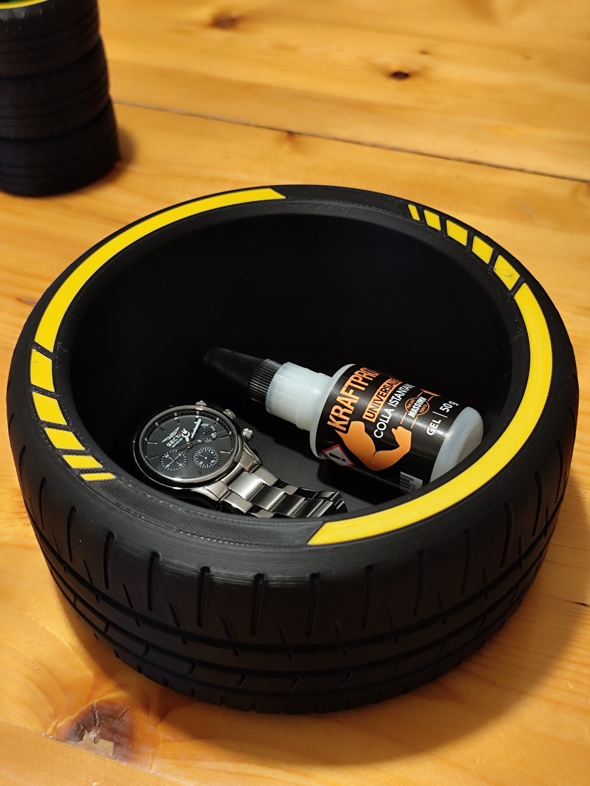 Black tire catchall bowl with yellow accents holding a watch and small bottle